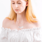 A woman with blonde hair wearing an off-the-shoulder white top and a silver necklace with three interconnected sloth pendants engraved with names.