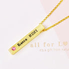 A gold necklace with a vertical bar pendant engraved with "Bianca 10.13.02" and a pink gemstone, placed on a card with partial text "all for L♥ve, it's a gift from nature."