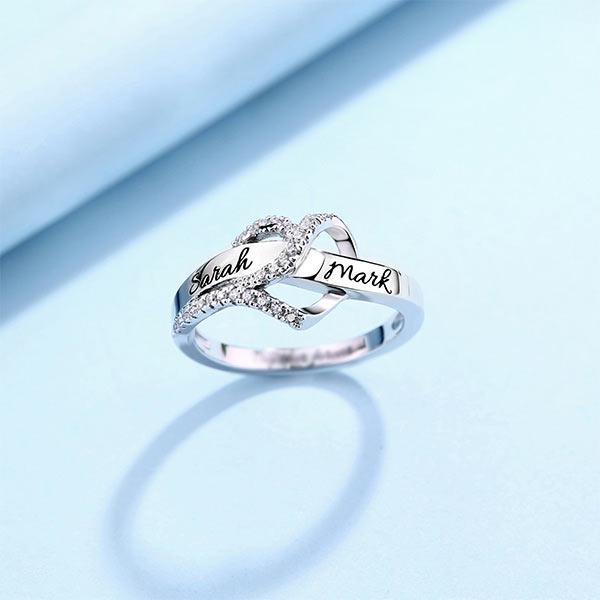 Custom infinity ring with 'Sarah' and 'Mark' engraved on a shimmering cubic zirconia band, presented on a blue backdrop