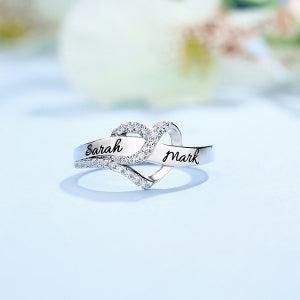 Silver infinity ring personalized with 'Sarah' and 'Mark' engraved, set against a serene blue background