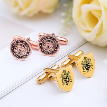 A pair of rose gold and a pair of gold cufflinks, each with embossed emblems, on a white background with a yellow rose.