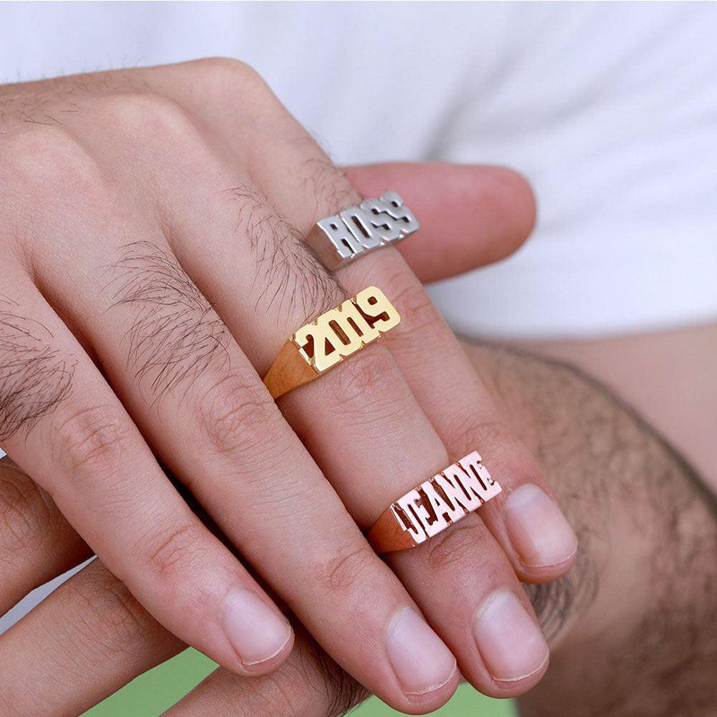 Three custom block name rings on fingers, in silver, gold, and rose gold, with 'BOSS', '2019', and 'JEANNE' engraved.