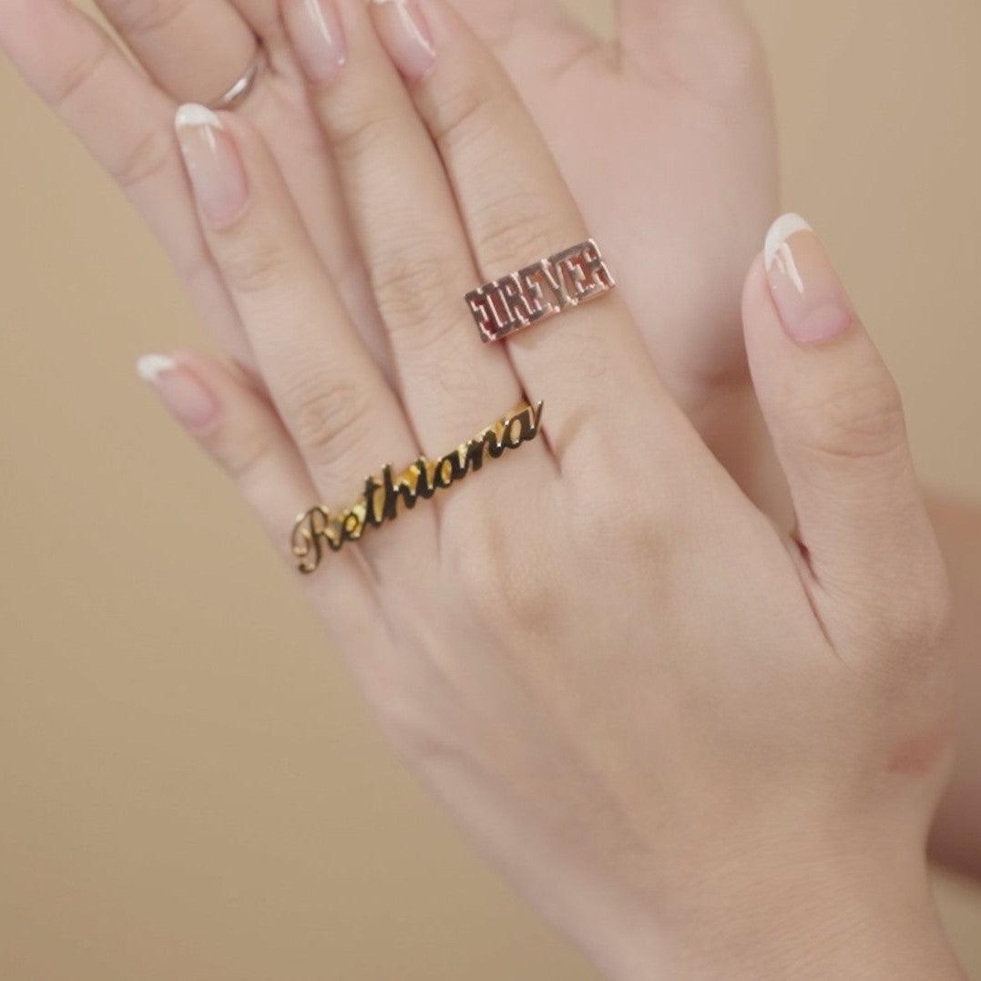 Hand wearing two-finger rings with 'Charlotte' in rose gold and 'Bethany' in gold, elegant personalized jewelry.