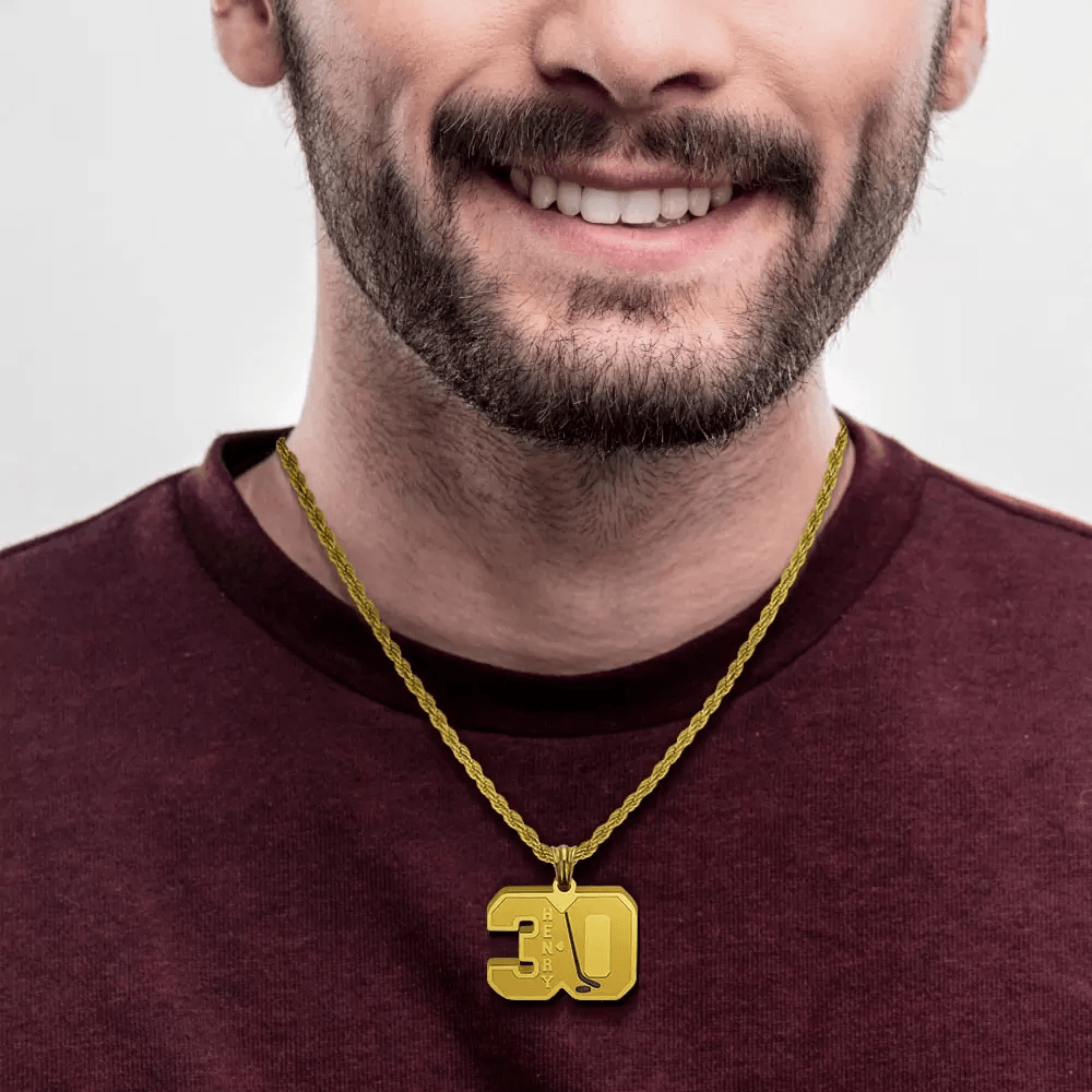 A smiling man wearing a maroon shirt, showcasing a gold hockey-themed necklace with the name "HENRY" and number 30.