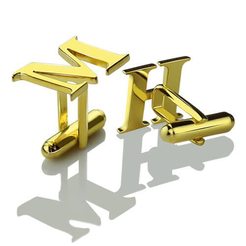 Gold initial cufflinks with the letters 'MH' on a reflective white surface casting distinct shadows.