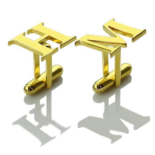 Gold initial cufflinks with the letters 'HM' on a reflective white surface casting sharp shadows.