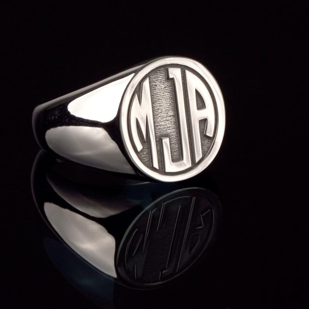 Sophisticated silver signet ring displaying 'MJA' monogram initials, set against a dark reflective backdrop.