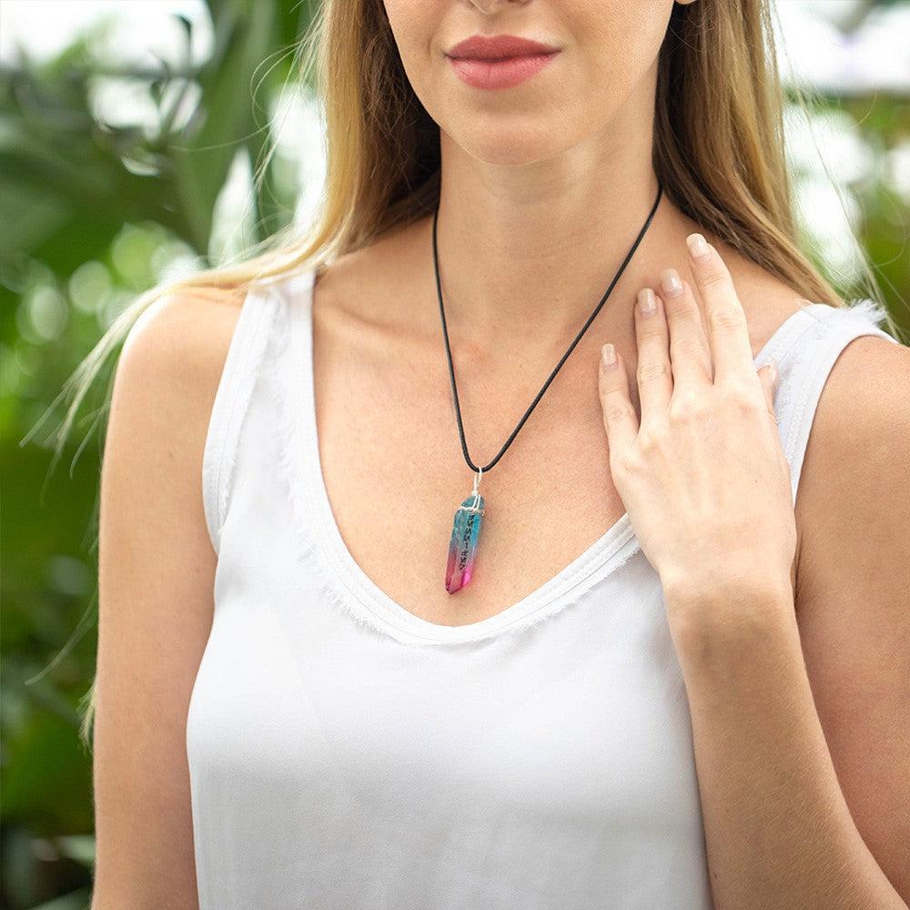 Woman wearing a white tank top and a kyber crystal necklace with pink and blue hues.