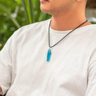 Man in white shirt with a blue kyber crystal necklace featuring Aurebesh inscription.