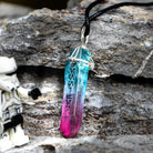 Kyber crystal necklace with Aurebesh, beside a figurine on a rocky surface.