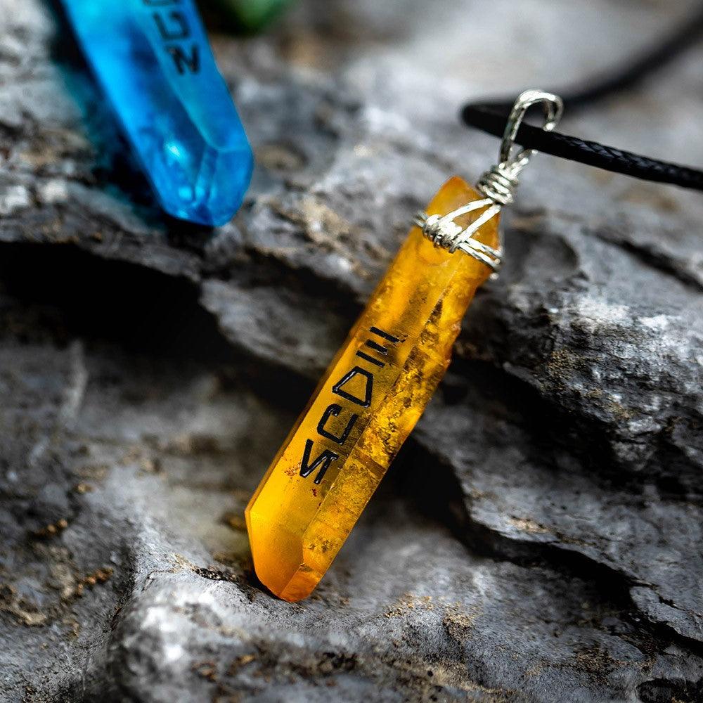 Yellow Kyber crystal pendant with black Aurebesh text on a rocky background.