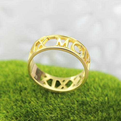 A gold sculpted cut-out style ring with the Roman numerals "MCMXIX" (1919) prominently displayed, placed on a green surface.