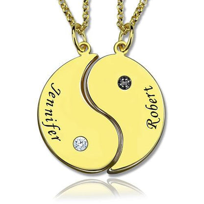 A gold yin-yang necklace with two separate chains; each half has a name engraved ("Jennifer" on the left and "Robert" on the right) and a gemstone embedded.