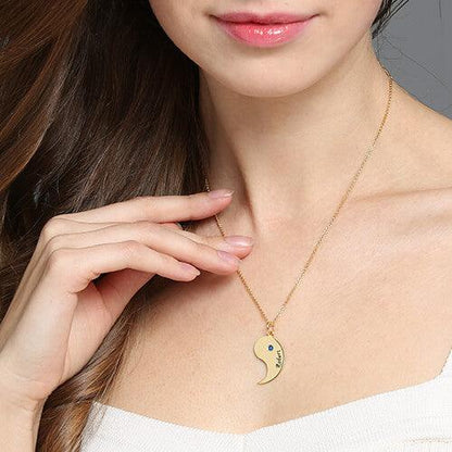 A woman wearing a white top and a single half of a gold yin-yang necklace with an embedded gemstone and the name "Robert" engraved on it.