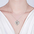 Woman wearing a silver heart-shaped necklace pendant featuring baby feet, engraved with the name "Peyton" and the date "07.22.2008," adorned with a pink gemstone.