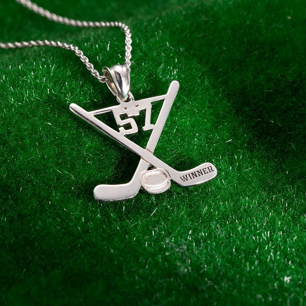 Silver hockey necklace pendant with the number 57 and "WINNER" tag on a twist chain, displayed on a green background.