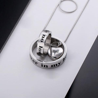 Silver necklace with interlocking rings and heart pendant engraved 'Dad', displayed on a sleek, modern background.