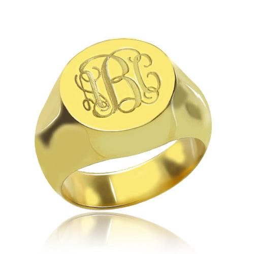 A polished gold signet ring with engraved ornate initials "LBC" on its flat top surface.
