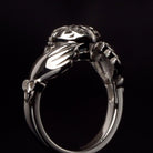 Side view of a silver Claddagh ring showcasing detailed hands and crowned heart design on a dark background.