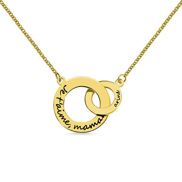 A gold necklace with interlocking circles. The larger circle has "Je t'aime, maman" engraved, and the smaller circle has the name "Aria" engraved.