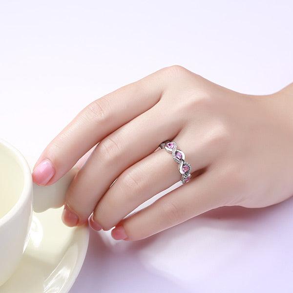A hand wearing a silver ring with pink gemstones in a twisted design, holding a white teacup on a saucer.