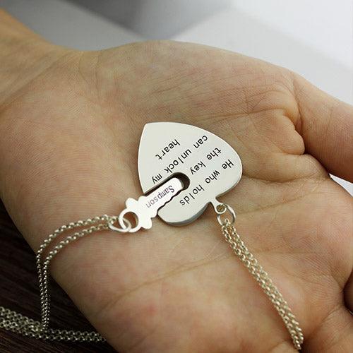 A hand holding a heart-shaped pendant necklace with the engraved message: "He who holds the key can unlock my heart" and a key-shaped charm, both attached to separate chains.