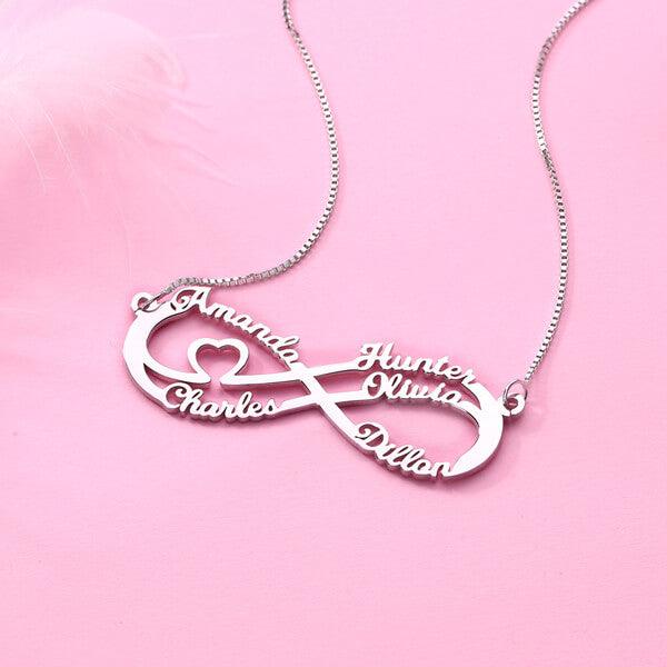 Silver double infinity necklace featuring the names Amanda, Charles, Hunter, Olivia, and Dillon in a delicate script, with a small heart, displayed on a pink background.