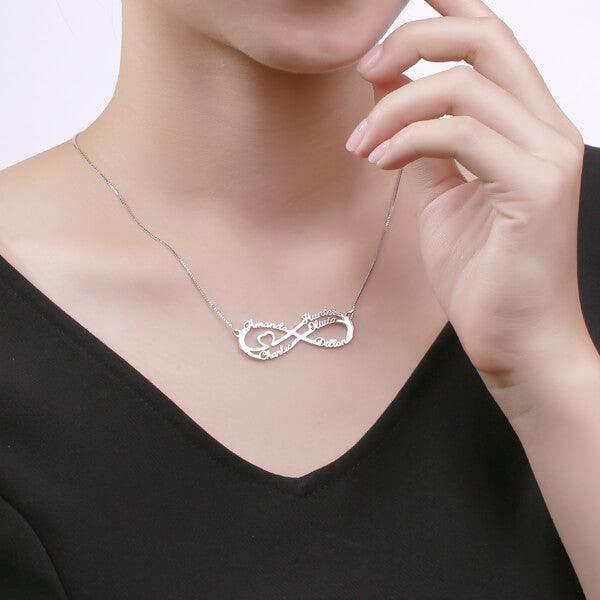 Woman wearing a silver double infinity necklace featuring the names Amanda, Charles, Hunter, Olivia, and Dillon in a delicate script, with a small heart in the design.