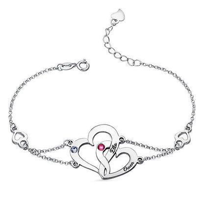 A silver bracelet featuring two intertwined hearts with the names Ella and Owen, adorned with a red and a blue gemstone, and heart-shaped links on the chain.