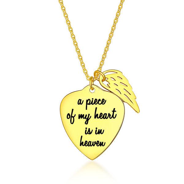 A gold necklace with a heart-shaped pendant engraved with "a piece of my heart is in heaven" and an angel wing charm against a white background.