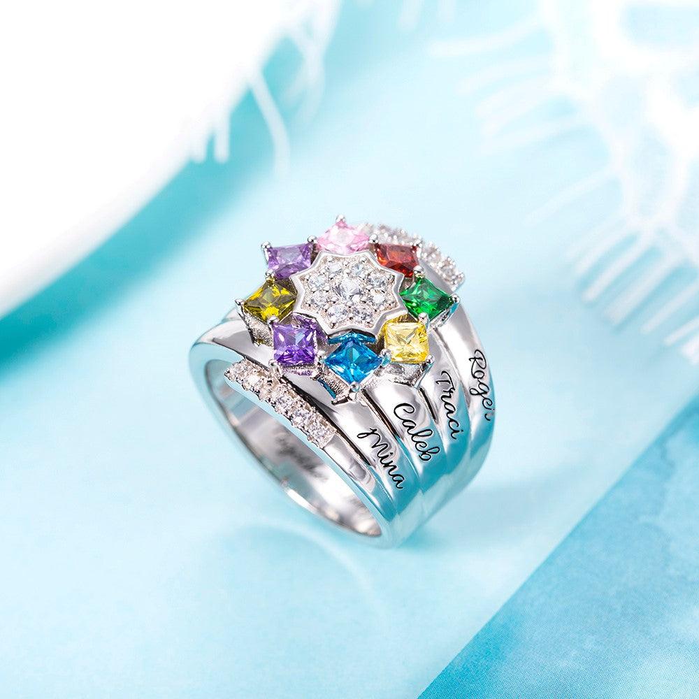 A silver ring adorned with colorful gemstones arranged in a star shape, featuring engraved names on its band and additional small diamonds on the sides.