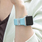 Person wearing an Apple Watch with a light blue band and personalized silver charms featuring the name "Connor" and diamond-like accents.