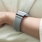 Person wearing an Apple Watch with a gray band and personalized black and silver charms featuring the name "Milroy" and diamond-like accents.