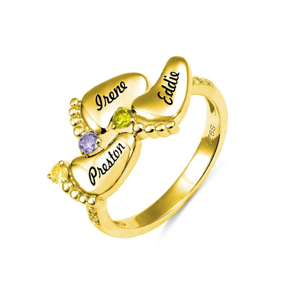 A gold ring featuring four engraved baby feet with names "Irene," "Eddie," "Preston," and "Amber," adorned with colorful gemstones, symbolizing "Always in my heart."