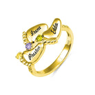 A gold ring featuring four engraved baby feet with names "Irene," "Eddie," "Preston," and "Amber," adorned with colorful gemstones, symbolizing "Always in my heart."