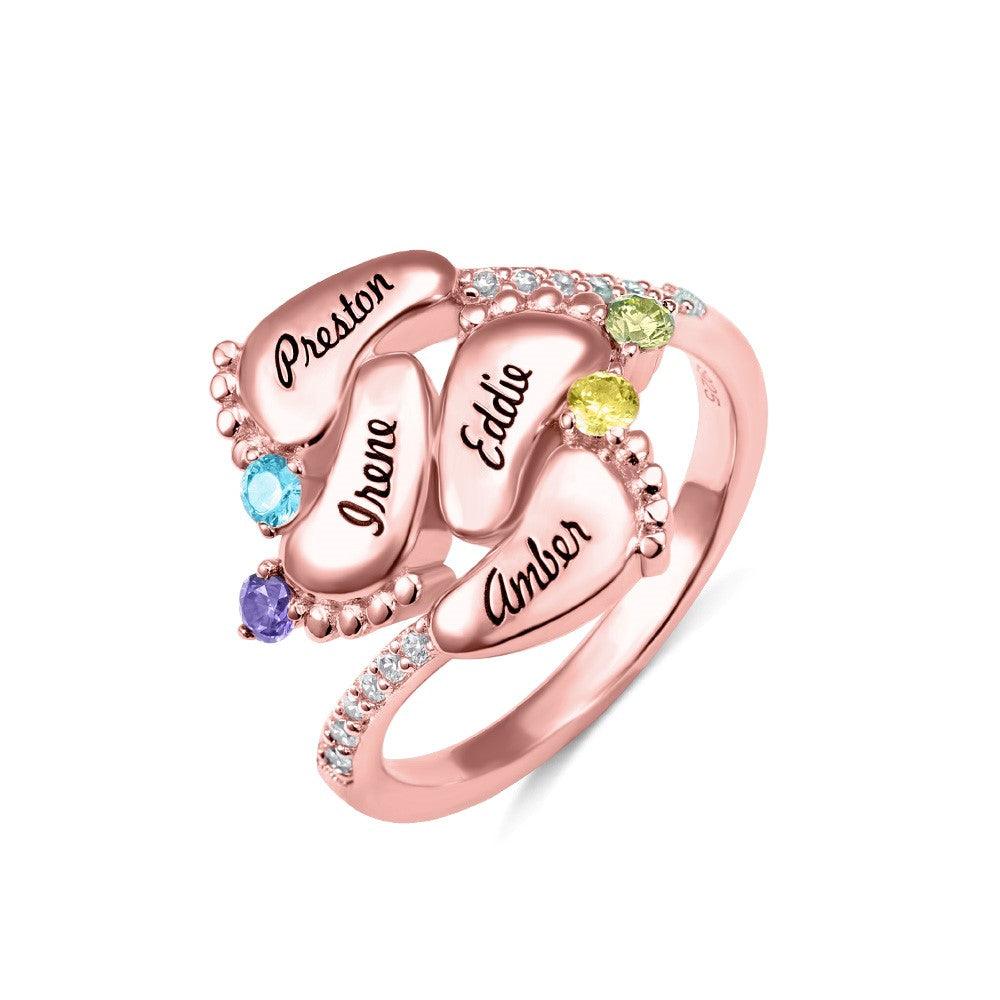 A rose gold ring featuring four engraved baby feet with names "Preston," "Irene," "Eddie," and "Amber," adorned with colorful gemstones, symbolizing "Always in my heart."