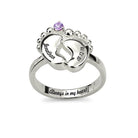 A silver ring with two engraved baby feet, featuring the name "Jonathan" and birth date "8.12.10" with a purple gemstone and the inscription "Always in my heart."