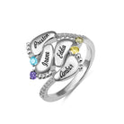 A silver ring featuring four engraved baby feet with names "Preston," "Irene," "Eddie," and "Amber," adorned with colorful gemstones, symbolizing "Always in my heart."