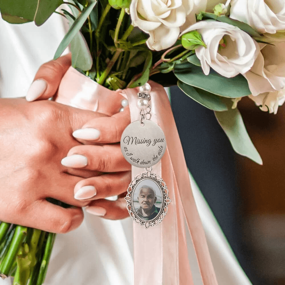 Bride's hand holding a bouquet with a 'Missing you' memorial photo charm.