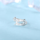 Silver ring with cut-out names "Emma" and "Noah" in cursive, placed on a light blue surface with a soft-focus background.