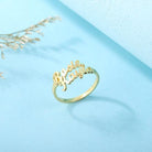 Gold ring with cut-out names "Rosie" and "Kayla" in cursive, placed on a light blue surface with decorative dried branches in the background.