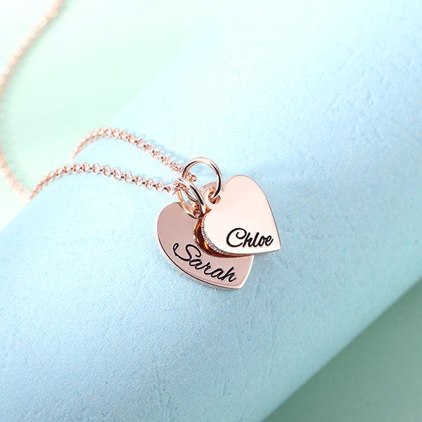 A rose gold necklace with two heart-shaped pendants, one engraved with "Sarah" and the other with "Chloe," displayed on a light blue background.