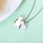 A silver necklace with two heart-shaped pendants, one engraved with "Sarah" and the other with "Chloe," displayed on a light green background near a fluffy item.