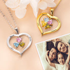 Two heart-shaped necklaces, one silver and one gold, with colorful birthstones and engraved names, displayed beside a happy family photo and delicate flowers.