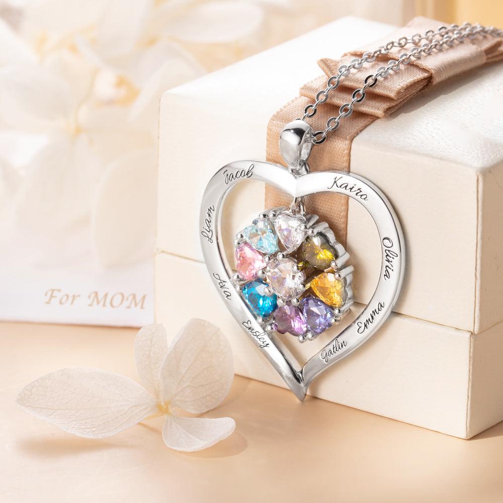 A heart-shaped silver necklace with colorful birthstones and engraved names, elegantly displayed on a gift box with a ribbon, and a note "For MOM."