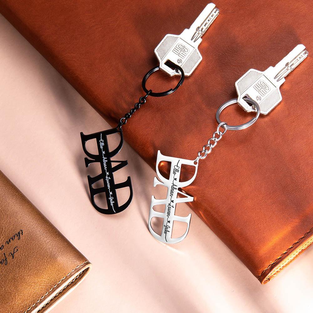 Two "DAD" keychains, one black and one silver, with personalized names, placed on a leather backdrop.