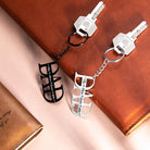 Two "DAD" keychains, one black and one silver, with personalized names, placed on a leather backdrop.