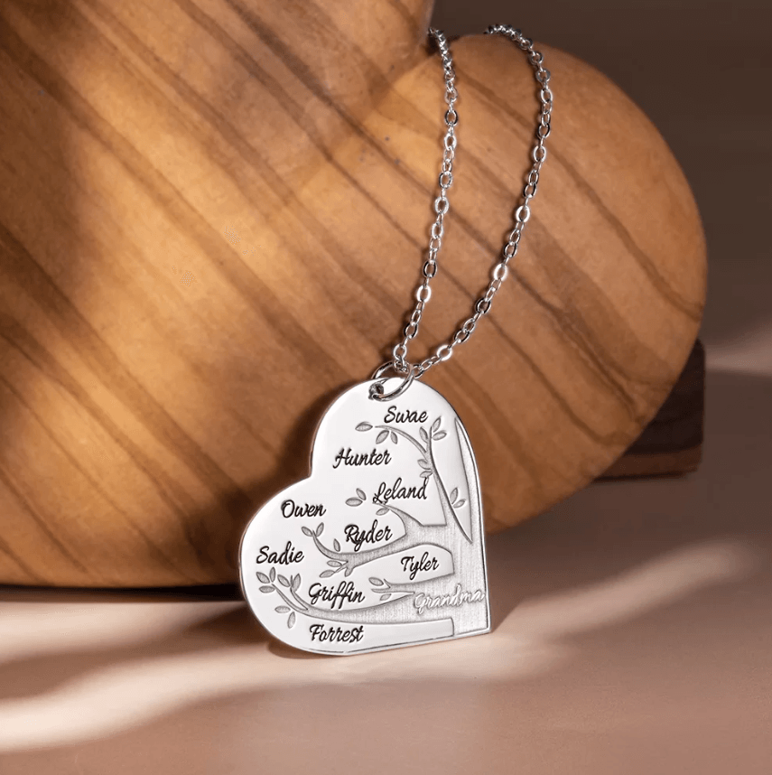 Silver heart-shaped pendant necklace with a family tree design, featuring names Surae, Hunter, Leland, Owen, Ryder, Tyler, Sadie, Griffin, Forrest, and "Grandma" at the bottom.