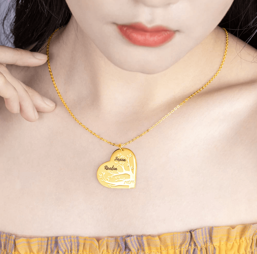 Woman wearing a gold heart-shaped pendant necklace with a family tree design, featuring names Jaxon, Raeden, and "mom" at the bottom.