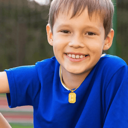 A smiling boy wearing a blue shirt and a gold number pendant with "8" and the name "Elijah" engraved on it, posing outdoors.